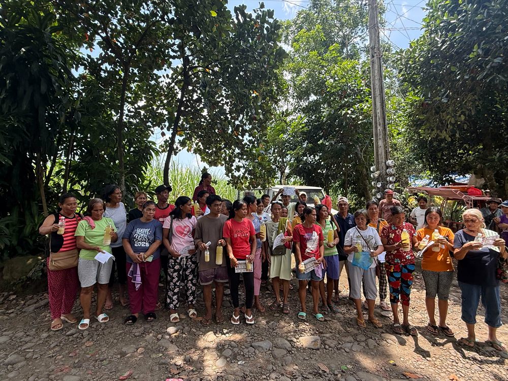A long line of farmers standing on a rural track, each holding a bottle of the biological control agent.